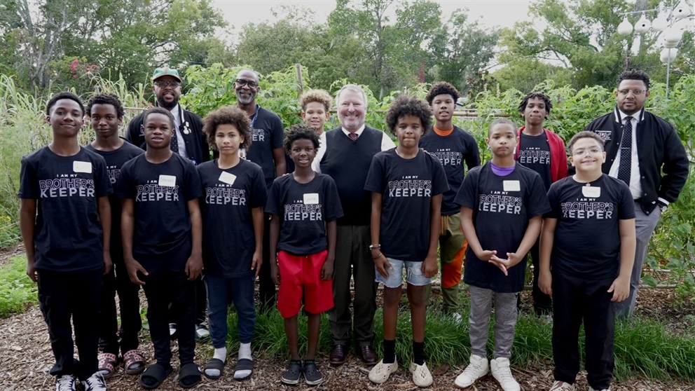 MBK participants and Mayor Dyer posing in front of a community garden